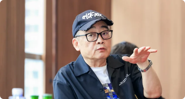 董克平戴黑色棒球帽与黑框眼镜，抬手比划讲菜，深色衬衫神态生动