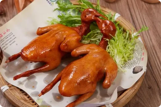 两只红烧脆皮乳鸽，色泽红亮油润，置于竹编蒸笼中