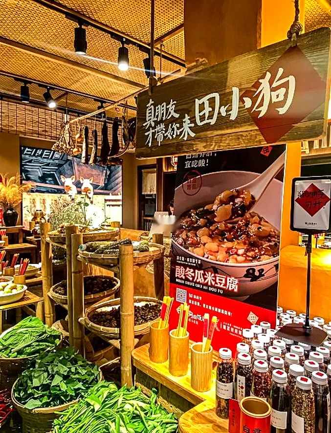 田小狗的明档食材台:竹编吊顶配黑色轨道射灯,灯只落在食材上,竹筐里是干货,上方吊着熏腊,下方一排有机调料瓶,竹筒里插着写菜名的竹签