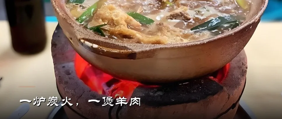 红泥炭炉上的一煲羊肉：带皮羊腩、蒜段与支竹在瓦煲里翻滚，炉中炭火正红